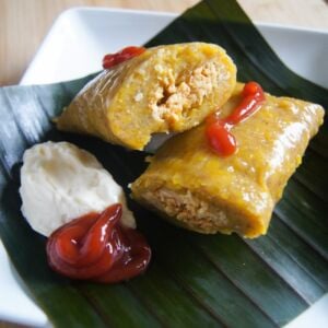 Pasteles en hoja served on a plate with a red and white sauce.