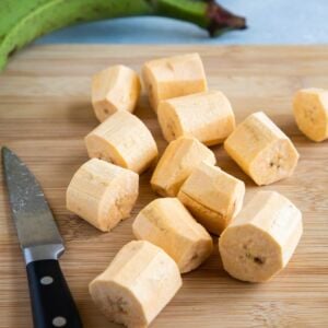 Green Plantains peeled and cut into 1 inch rounds on top of a kitchen wooden board.