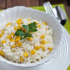 Rice and corn in a white bowl garnished with fresh cilantro.