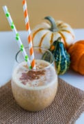 A pumpkin pie smoothie in a glass with two straws.