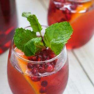 Pomegranate sangria in a glass garnished with a mint sprig.
