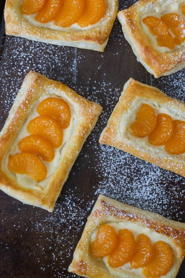 Mandarin and cheese pastelitos on a baking sheet dusted with powdered sugar.