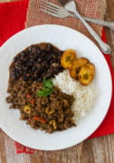 Beef picadillo served on a white plate with rice, plantains and beans.
