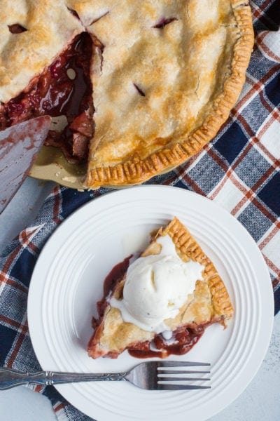 Apple and cranberry pie served with ice cream on a white plate.
