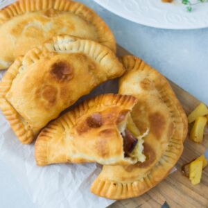 Ham and pineapple empanadas on a wooden serving board.