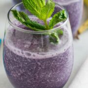 Blueberry banana oat smoothie in a glass with a mint sprig.