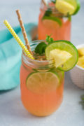 A cherry pineapple mojito in a glass mason jar with two straws and lime slice garnish.