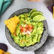 Guacamole served in a bowl with a tortilla chip and fresh lime slices.