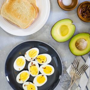 Hard boiled eggs on a black plate next to toast and avocado
