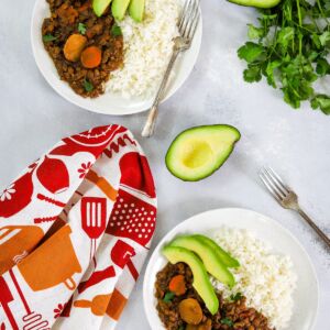 Slow cooker lentil stew served in two bowls with rice and sliced avocado.
