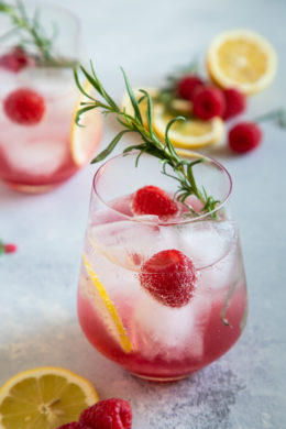 raspberry lemon wine spritzer served in a glass with lemon slices, raspberries and rosemary for garnish