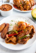 Pollo guisado served on a white plate with rice and garnished with fresh herbs.