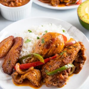 Dominican Braised Chicken or Pollo Guisado served on a plate with white rice, beans and maduros