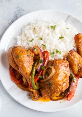 Dominican Braised Chicken or Pollo Guisado served on a plate with white rice, beans and maduros