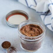 Homemade taco seasoning in a glass jar next to a blue and white cloth.