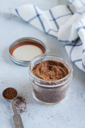 Homemade taco seasoning in a glass jar next to a blue and white cloth.