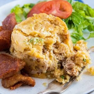 Mofongo servido en un plato blanco con ensalada y chicharrón