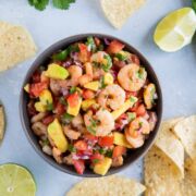 Overhead shot of shrimp salsa in a large bowl next to tortilla chips and lime wedges.