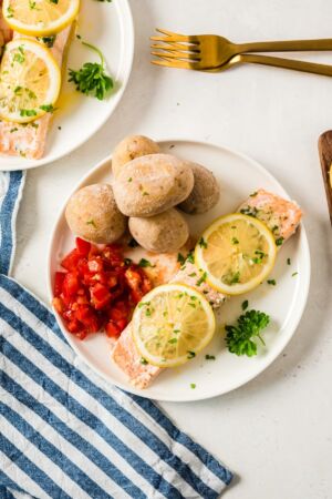 A fillet of salmon on a white plate, topped with lemon slices and served with potatoes.