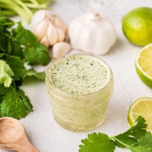 A wooden spoon next to a jar of cilantro dressing
