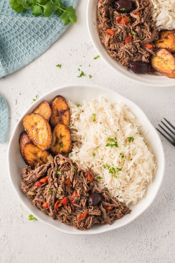 Shredded beef served in two bowls with rice and plantain
