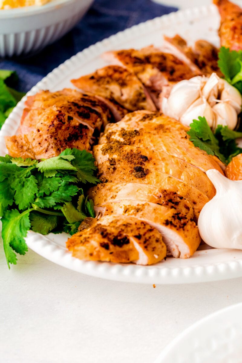 Pieces of carved turkey on a plate with fresh herbs and garlic bulbs