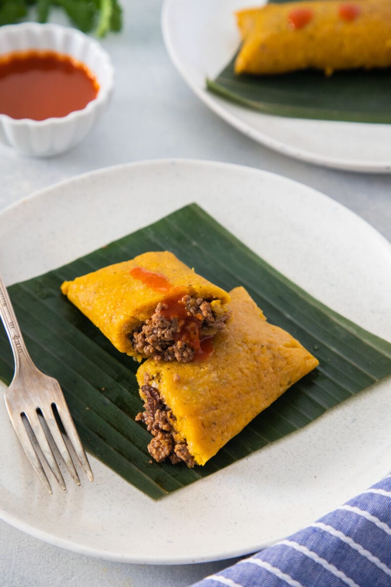 a pastel en hoja served on a plate topped with hot sauce