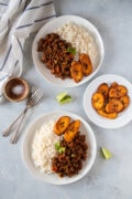 Two plates of picadillo served with rice and plantains