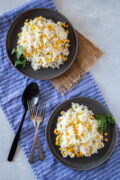 Rice with corn served in two gray plates with forks on the side