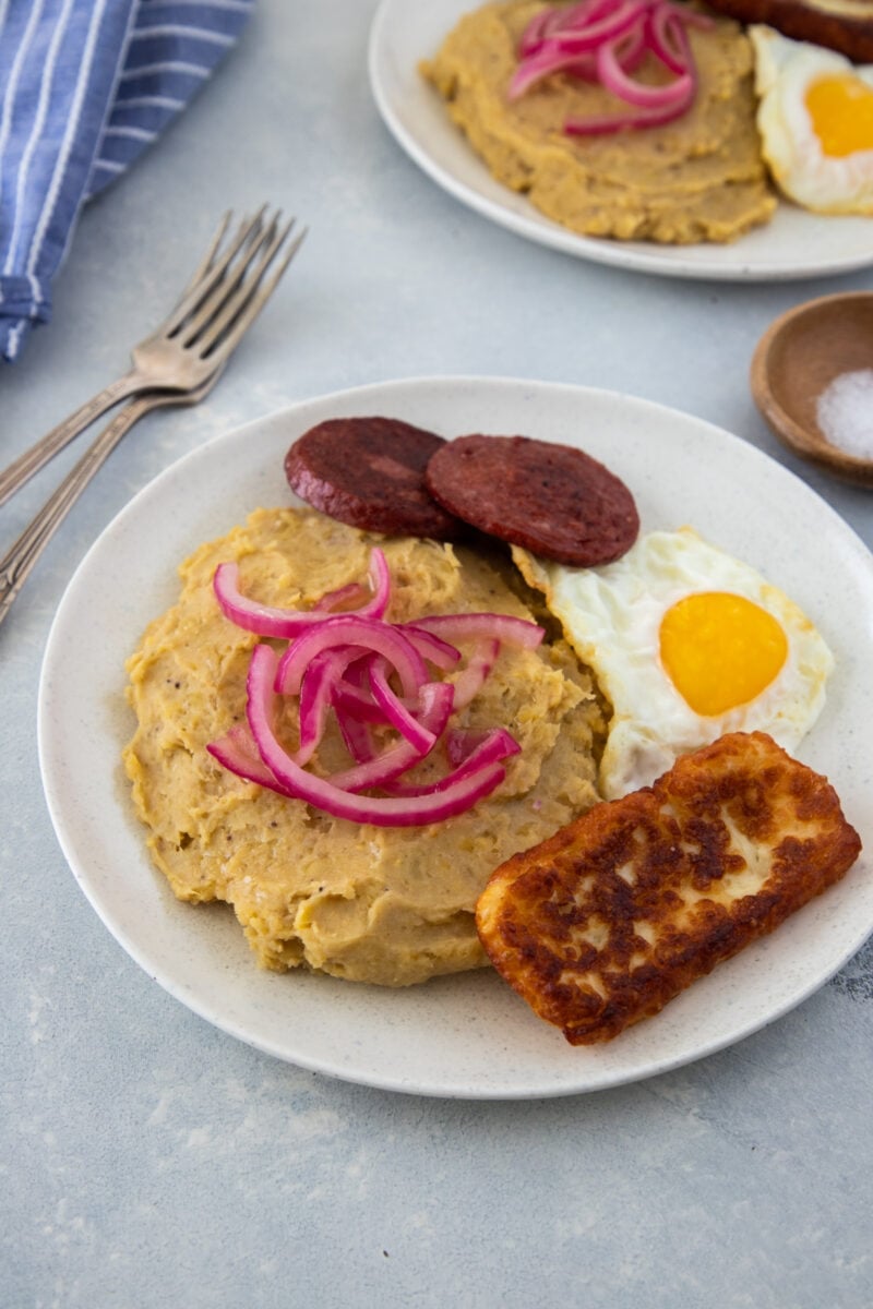 Mangu topped with onions and served with fried egg, salami and fried cheese