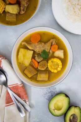 Sancocho served in a white bowl with rice and avocado on the side