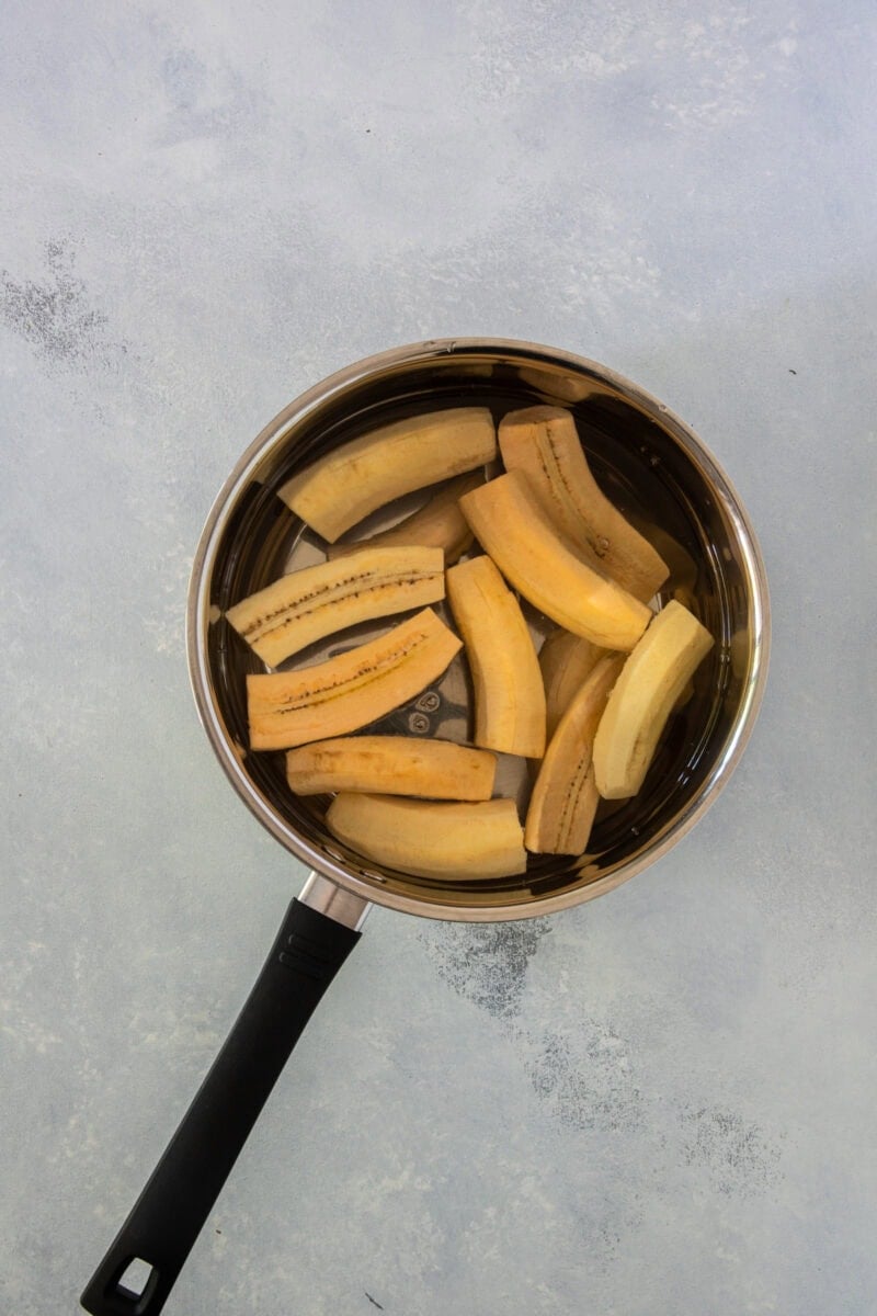 Plátanos verdes pelados y cortados en trozos, en una olla con agua.