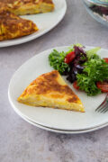 slice of Spanish omelette on a plate with salad on the side