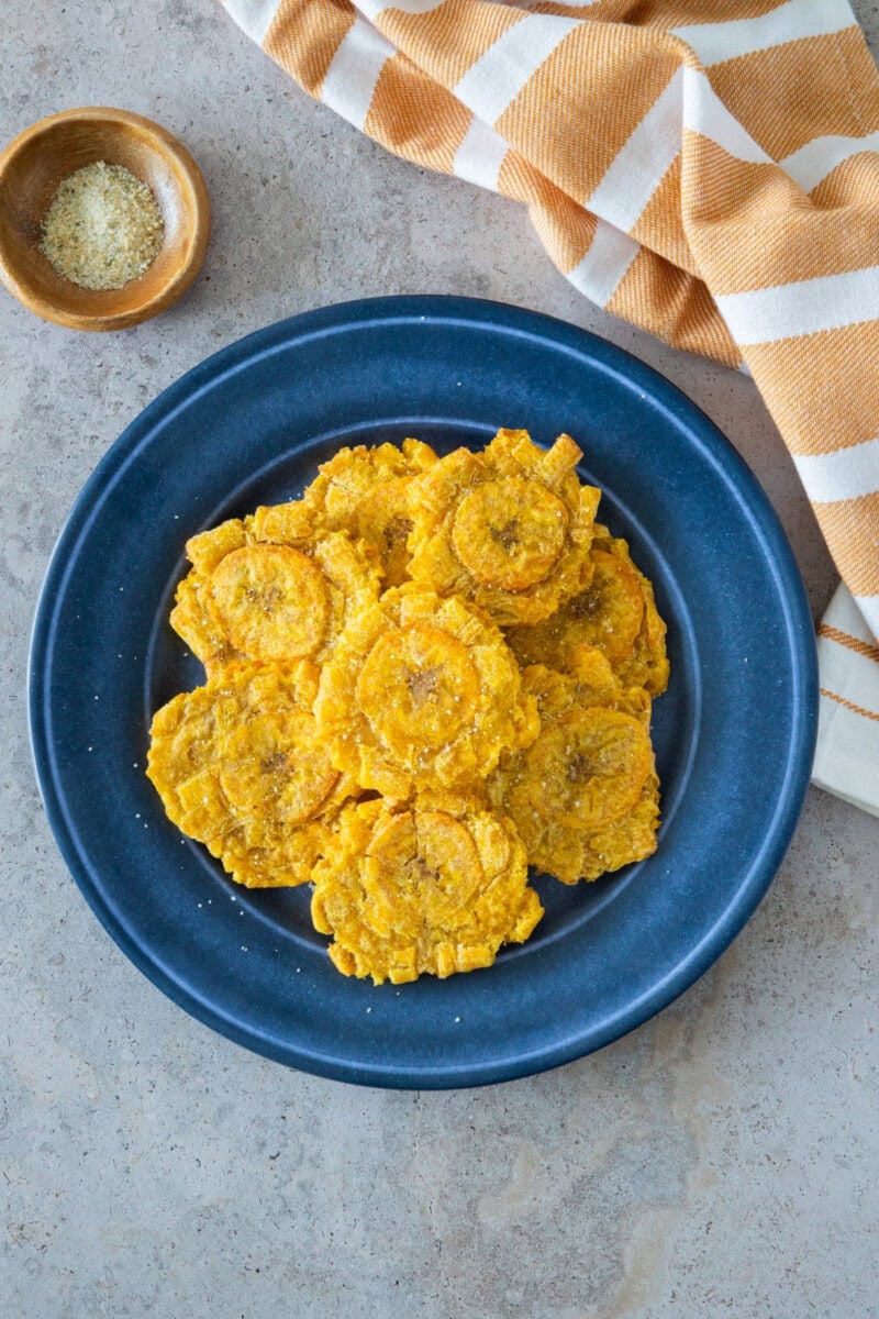 Air fryer tostones served in a blue plate with sea salt on the side