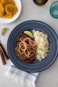A beef steak topped with onions, served with white rice and a lime wedge, ready to eat.
