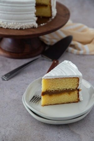Slice of Dominican vanilla cake with dulce de leche filling and white meringue frosting on a plate.