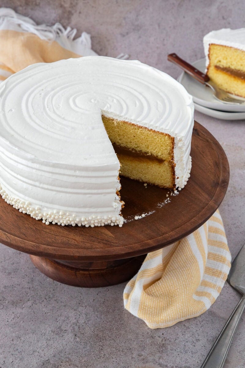 Bizcocho dominicano relleno de dulce de leche y cubierto con suspiro blanco sobre una base de madera.