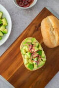 Avocado toast with red onion on rustic bread, served on a wooden board.