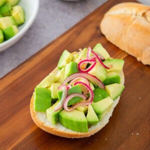 Avocado toast with red onion on rustic bread, served on a wooden board.