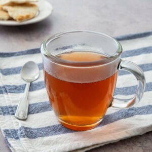 Ginger cinnamon tea in a glass mug on a striped cloth with a spoon.