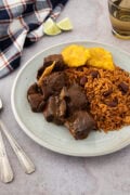 Plate of Dominican chivo guisado (braised goat stew) served with moro rice and beans and fried tostones
