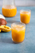 Two glasses of chilled passion fruit juice (jugo de chinola) with ice, served with fresh passion fruit on the side.
