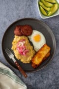 Dominican mangú with fried egg, salami, cheese, and pickled onions, served with avocado on the side.