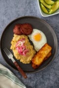 Dominican mangú with fried egg, salami, cheese, and pickled onions, served with avocado on the side.