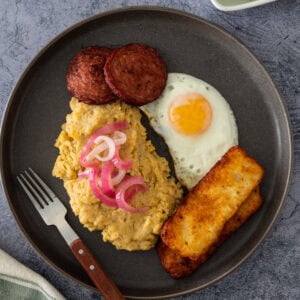 Dominican mangú with fried egg, salami, cheese, and pickled onions, served with avocado on the side.