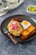 Dominican mangú with fried egg, salami, cheese, and pickled onions, served with avocado on the side.