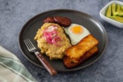 Dominican mangú with fried egg, salami, cheese, and pickled onions, served with avocado on the side.