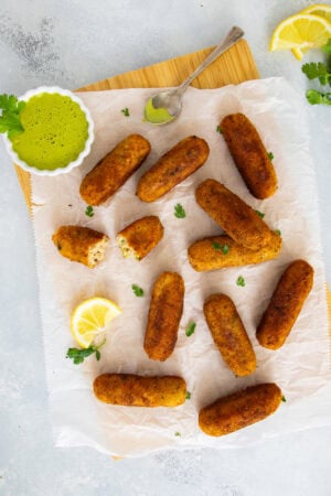 Golden tuna and potato croquettes served on parchment with creamy cilantro dipping sauce and a lemon wedge.