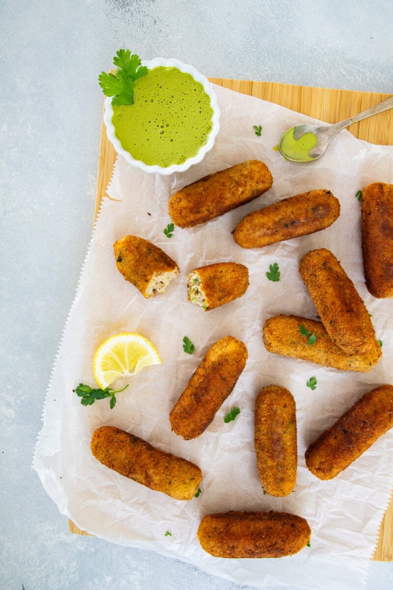 Croquetas doradas de atún y patata servidas sobre papel pergamino con salsa cremosa de cilantro para mojar y una rodaja de limón.